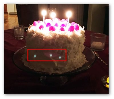 Ghost example: Photo taken with a cell phone camera that clearly shows three sharply focused ghost images of the candle flames. There is also a fourth, extended ghost image centered on the middle sharp ghost image.