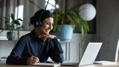 Happy young indian girl with wireless headphones looking at laptop screen, reading listening online courses, studying remotely from home due to pandemic corona virus world outbreak, quarantine time.